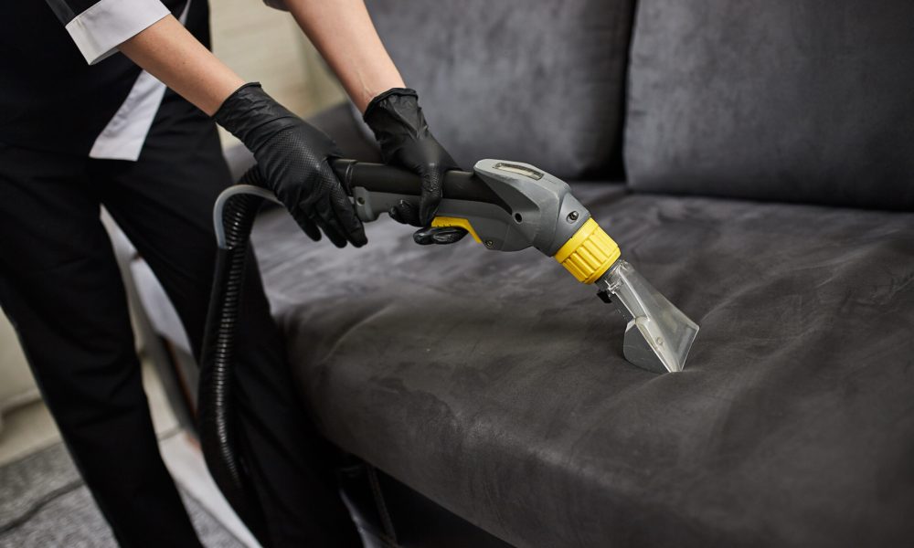 Cleaning service company employee removing dirt from furniture in flat with professional equipment. Female housekeeper arm cleaning sofa with washing vacuum cleaner close up